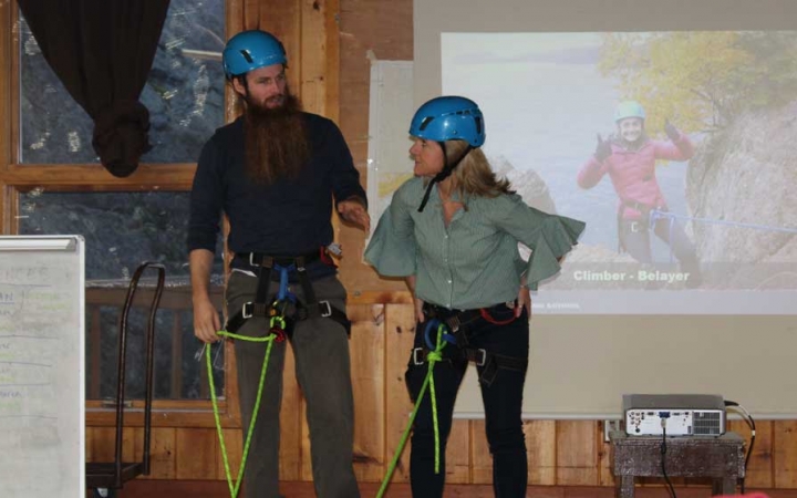 Two people stand inside, but in safety gear, in front of a screen displaying a presentation during the family seminar of an outward bound intercept course.